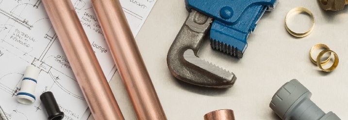 Diverse Materialen und Werkzeuge zum Verlegen von Rohren neben einem Bauplan.